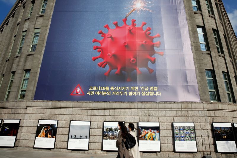 &copy; Reuters. Women wearing face masks walk past a banner promoting a social distancing campaign displayed on the wall of Seoul City Hall in Seoul