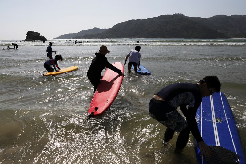 © Reuters. Surfers push their surfing boards as they head into the sea in Sanya