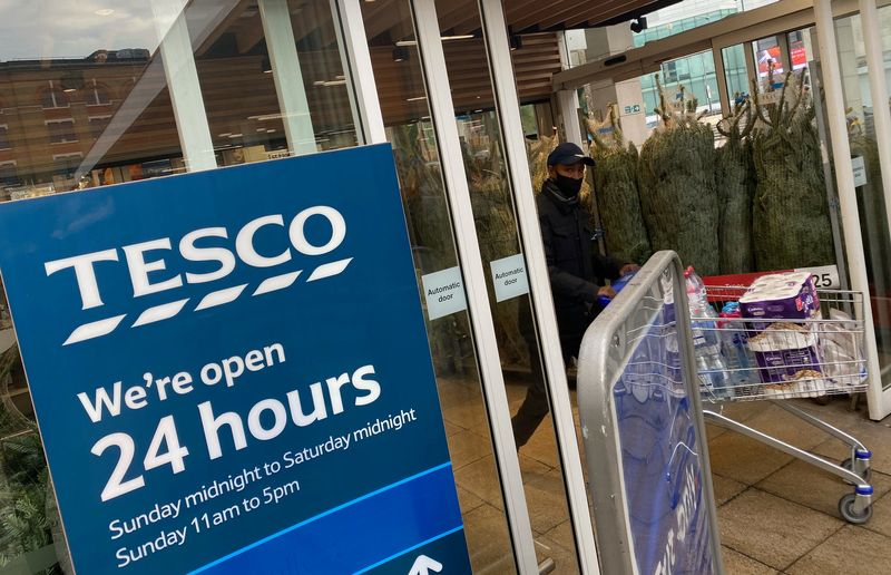 &copy; Reuters. Un comprador con mascarilla pasa por un cartel que indica los horarios de apertura de 24 horas en un supermercado Tesco en Londres, Reino Unido, 6 de diciembre de 2020