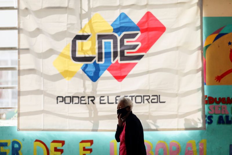 &copy; Reuters. Mulher passa em frente a faixa com o logo do Conselho Nacional Eleitoral em seção eleitoral em Caracas