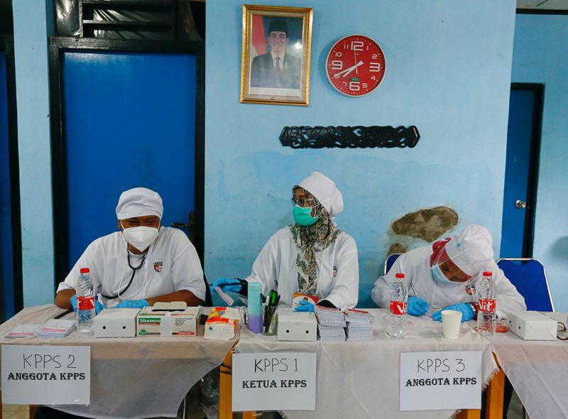 © Reuters. Officers wearing protective face masks work at a polling booth during regional elections in Depok