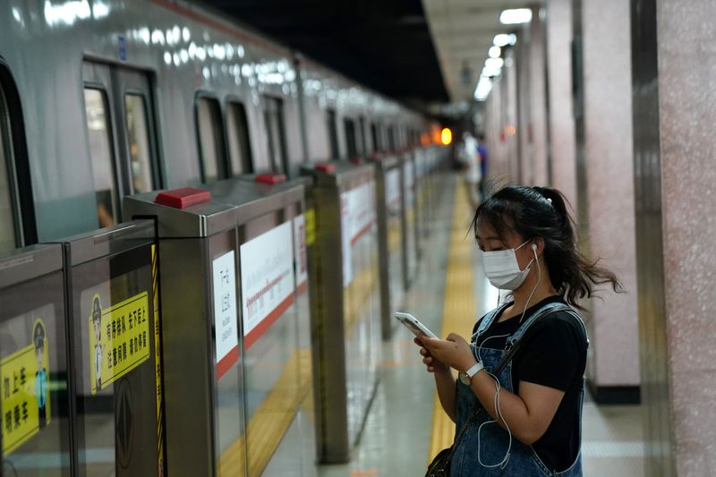 &copy; Reuters. Woman wearing a face mask following  coronavirus disease (COVID-19) outbreak looks at her smartphone while waiting for a subway in Beijing