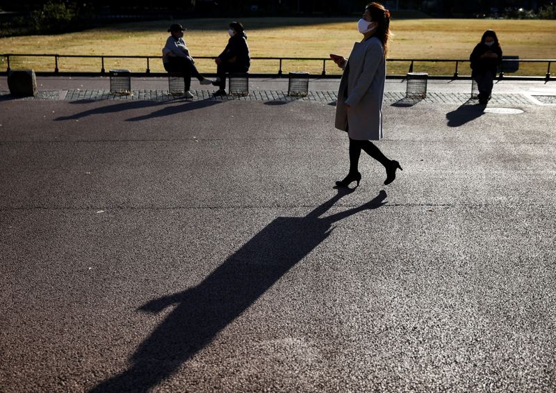 &copy; Reuters. Imagen de archivo. Una mujer con mascarilla camina frente los bancos de un parque en Tokio