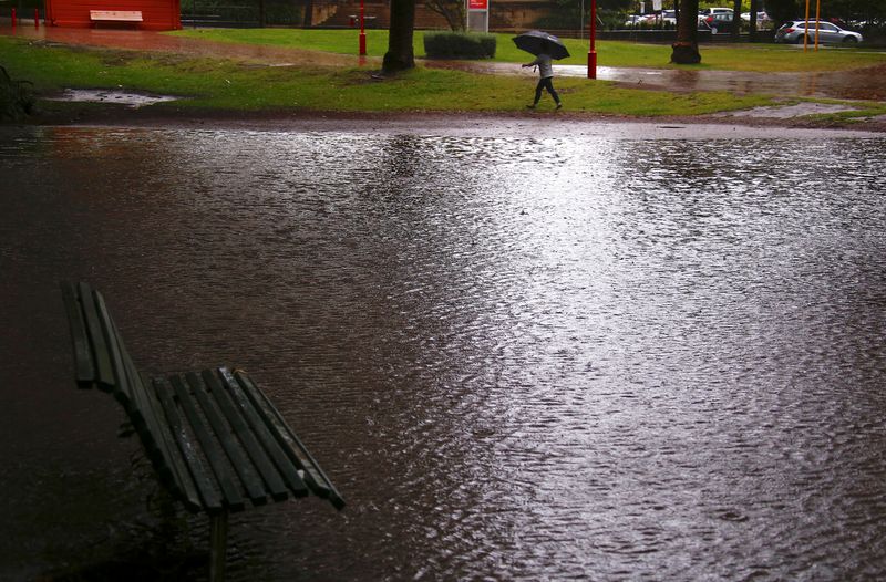 © Reuters. A woman carrying an umbrella walks past a flooded park as strong winds and floods cause traffic problems in Sydney