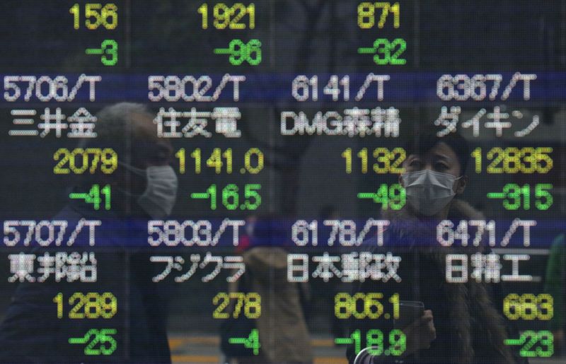 © Reuters. People wearing protective face masks are reflected in a stock quotation board outside a brokerage in Tokyo