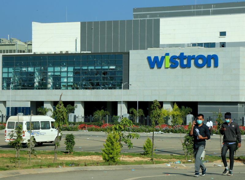 &copy; Reuters. Men wearing protective face masks walk past broken windows of a facility run by Wistron Corp in Narsapura