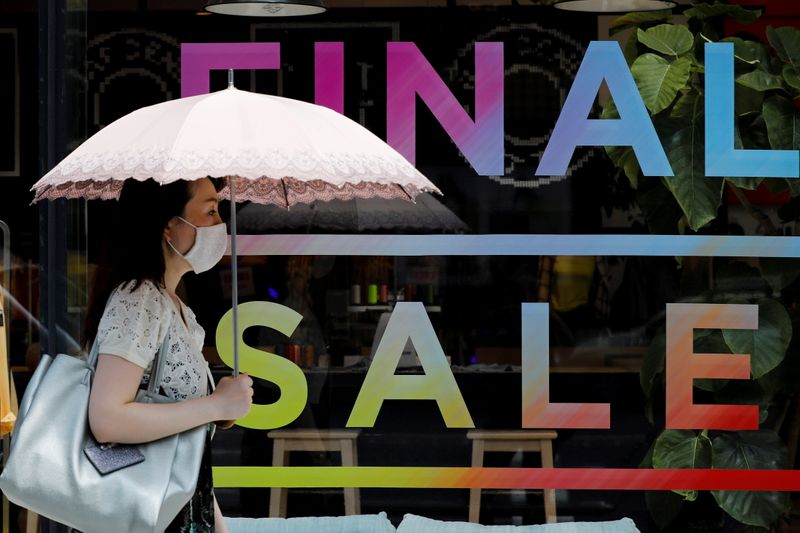 &copy; Reuters. FILE PHOTO: A woman wearing a protective face mask walks past a sign for a sale at a shopping district in Tokyo