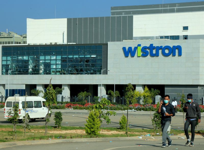 &copy; Reuters. FILE PHOTO: Men wearing protective face masks walk past broken windows of a facility run by Wistron Corp in Narsapura