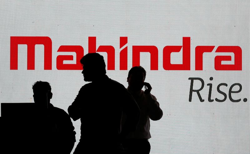 &copy; Reuters. People walk past a screen displaying Mahindra and Mahindra logo before the start of a news conference in Mumbai