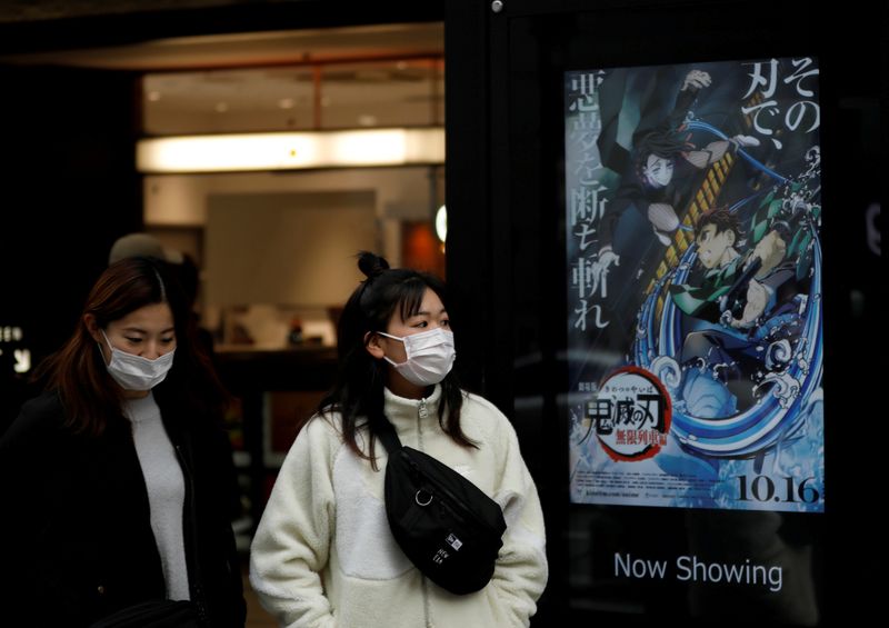 &copy; Reuters. FILE PHOTO: Women wearing protective masks amid the coronavirus disease (COVID-19) outbreak walk past a poster for an animated movie &quot;Demon slayer&quot; in front of a movie theatre in Tokyo