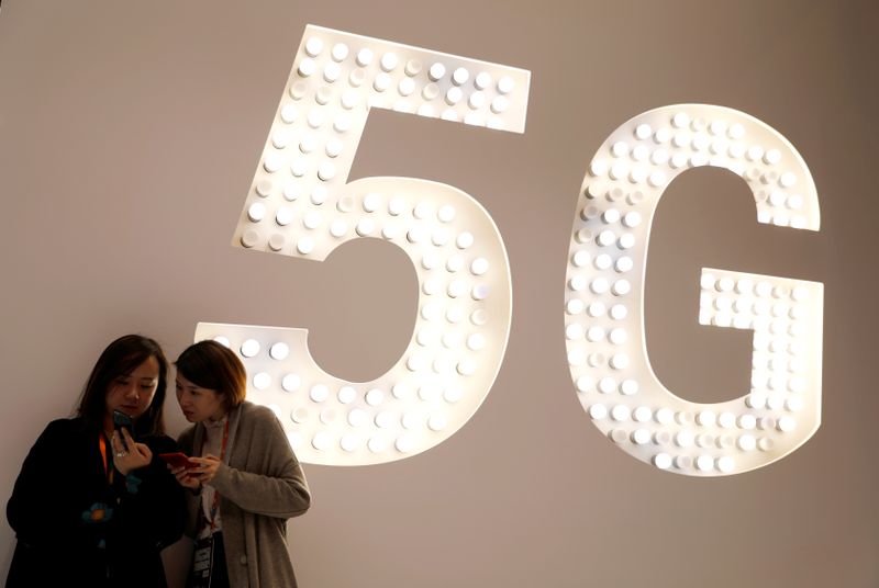 &copy; Reuters. Imagen de archivo de dos personas mirando sus móviles junto a una señal luminosa de la tecnología 5G en el stand de Xiaomi del Mobile World Congress en Barcelona, España.