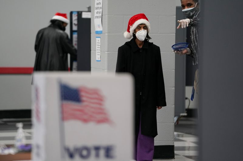 &copy; Reuters. FILE PHOTO:  A man points out hand sanitizer and disinfectant wipes to a voter after she cast her ballot in the U.S. Senate runoff elections on the first day of early voting in Atlanta