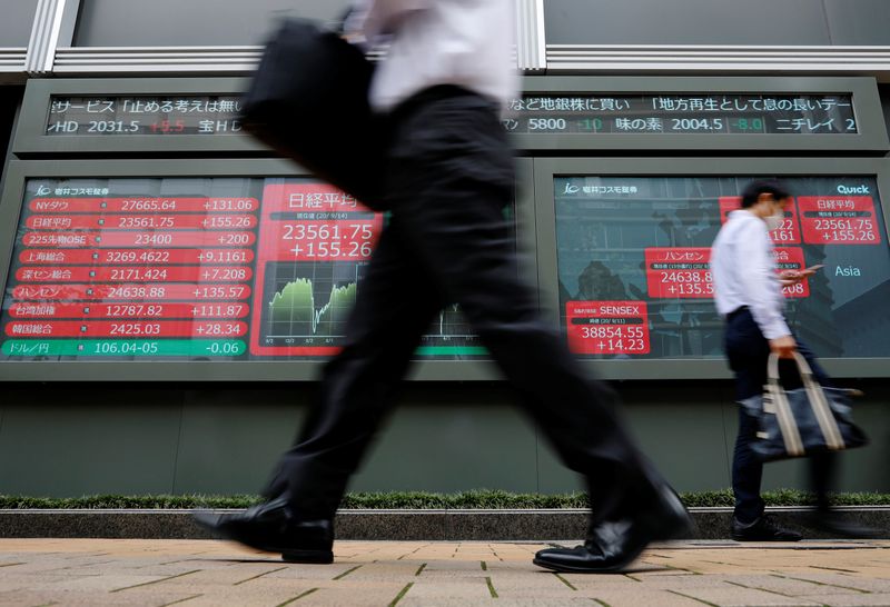 &copy; Reuters. Passersby wearing protective masks walk past an electronic board showing Japan&apos;s Nikkei average, in Tokyo