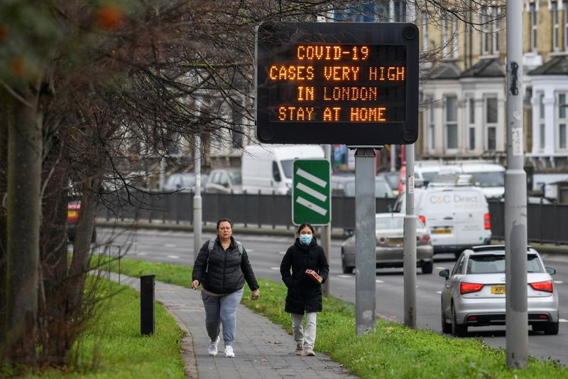 &copy; Reuters. People walk past a roadside public health information sign, amidst the coronavirus disease (COVID-19) pandemic, in London