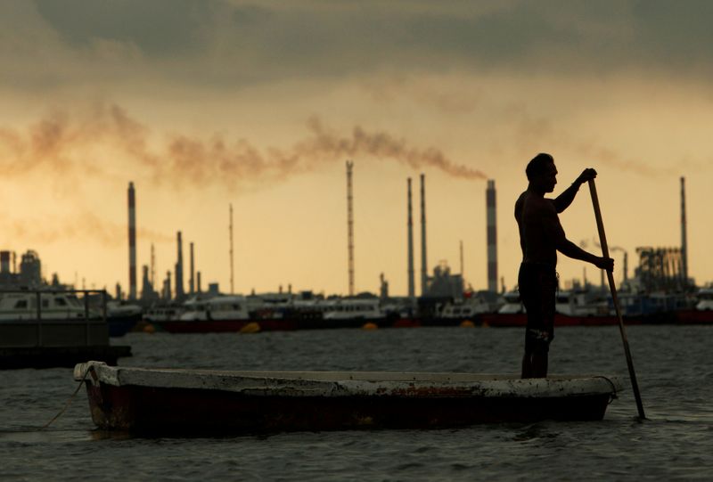&copy; Reuters. FILE PHOTO: A fisherman rows his dinghy past oil refineries near port terminals in Singapore