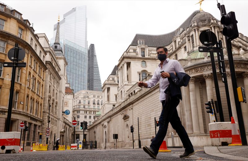 &copy; Reuters. A man wearing a face mask crosses the road in the City of London financial district amid the outbreak of the coronavirus disease (COVID-19)