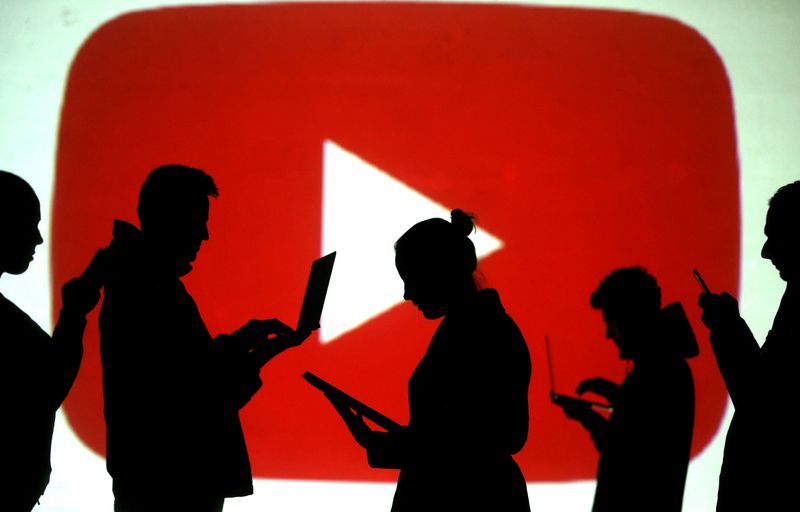 © Reuters. FILE PHOTO: Silhouettes of laptop and mobile device users next to a screen projection of the YouTube logo in this picture illustration