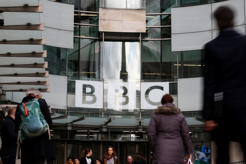 © Reuters. Pedestrians walk past a BBC logo at Broadcasting House, as the corporation announced it will cut around 450 jobs from its news division, in London