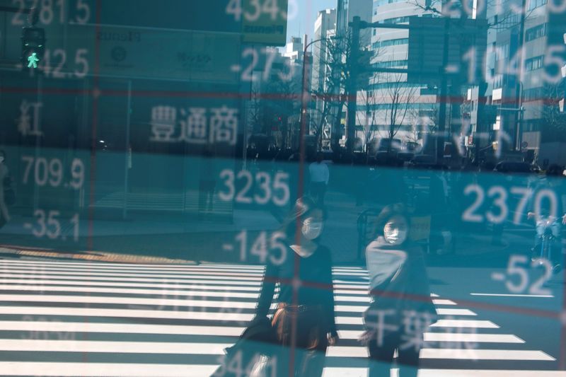 © Reuters. People wearing protective face masks, following an outbreak of the coronavirus, are reflected on a screen showing Nikkei index, outside a brokerage in Tokyo