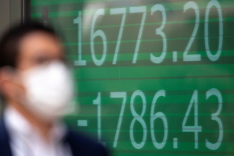 &copy; Reuters. A man wearing a protective face mask walks past a screen showing Nikkei index outside a brokerage in Tokyo
