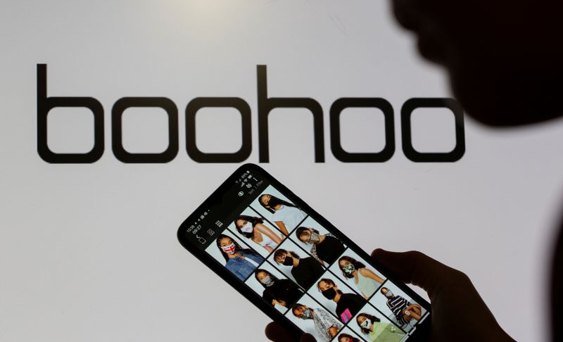 © Reuters. FILE PHOTO: A woman poses with a smartphone showing the Boohoo app in front of the Boohoo logo on display in this illustration