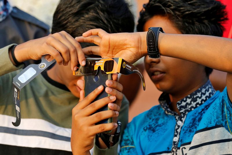 &copy; Reuters. FILE PHOTO: Boys use their mobile phone and solar viewers to take photographs of annular solar eclipse in Cheruvathur