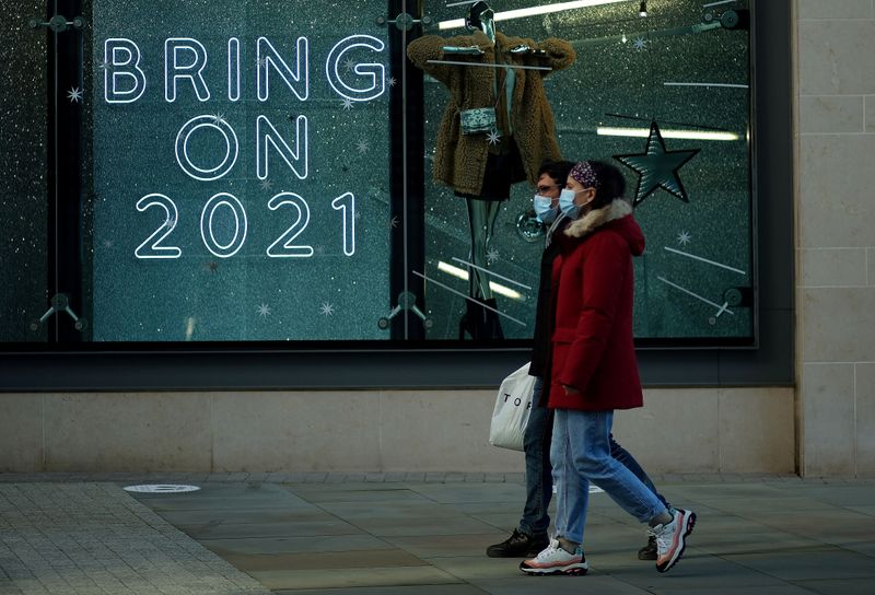 &copy; Reuters. FOTO DE ARCHIVO: Dos personas caminan frente al escaparate de una tienda en el que un cartel dice &quot;Que venga el 2021&quot; en inglés en Manchester