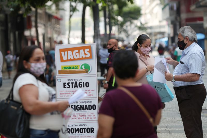 &copy; Reuters. Mulher entrega currículo à agente de recrutamento enquanto pessoas leem anúncios de vagas de emprego, no centro de São Paulo