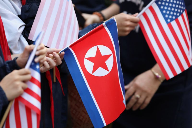 © Reuters. Bystanders holding North Korea and U.S. flags wait for the motorcade of U.S. President Donald Trump in Hanoi