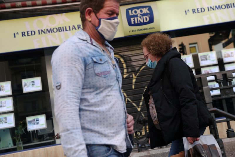 &copy; Reuters. FOTO DE ARCHIVO: Dos personas con mascarillas pasan por delante de una inmobiliaria en Madrid