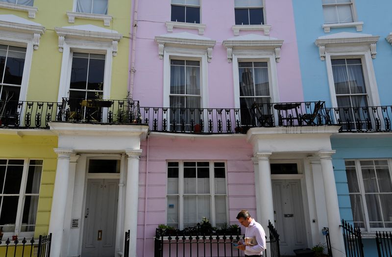 © Reuters. FILE PHOTO:  A man walks past houses painted in various colours in a residential street in London