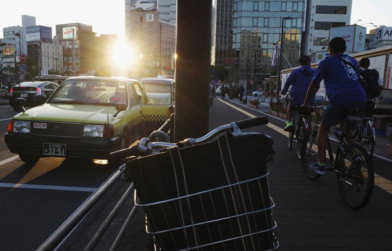 &copy; Reuters. Students ride bicycles past a taxi in Oita