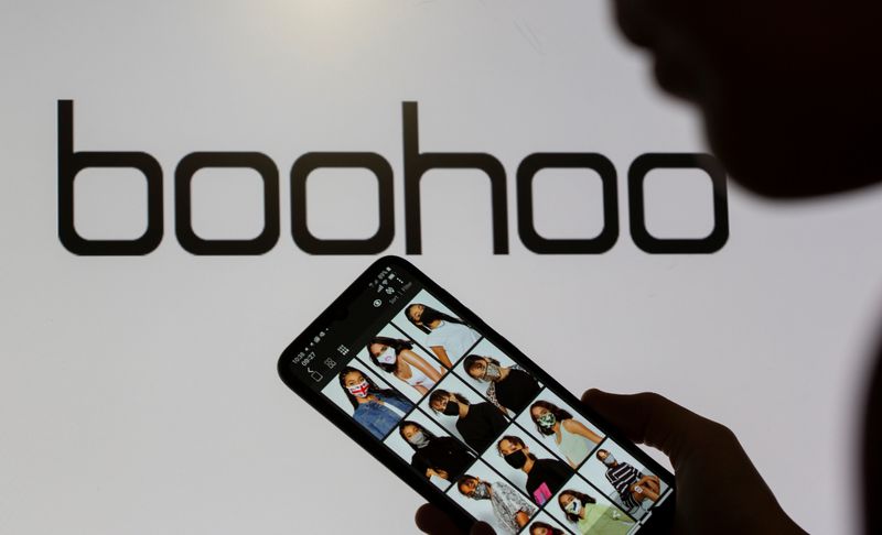 &copy; Reuters. A woman poses with a smartphone showing the Boohoo app in front of the Boohoo logo on display in this illustration