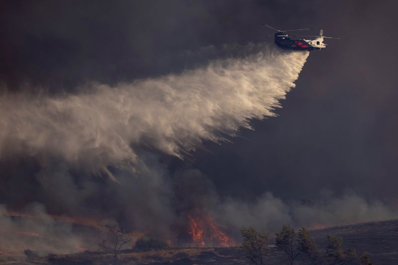 &copy; Reuters. FILE PHOTO: A helicopter makes a water drop on flames as firefighters battle the wind driven Bond Fire wildfire near Lake Irvine in Orange County, California