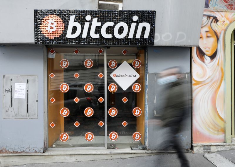 © Reuters. A man wearing a protective face mask walks past a Bitcoin digital currency ATM shop in Marseille