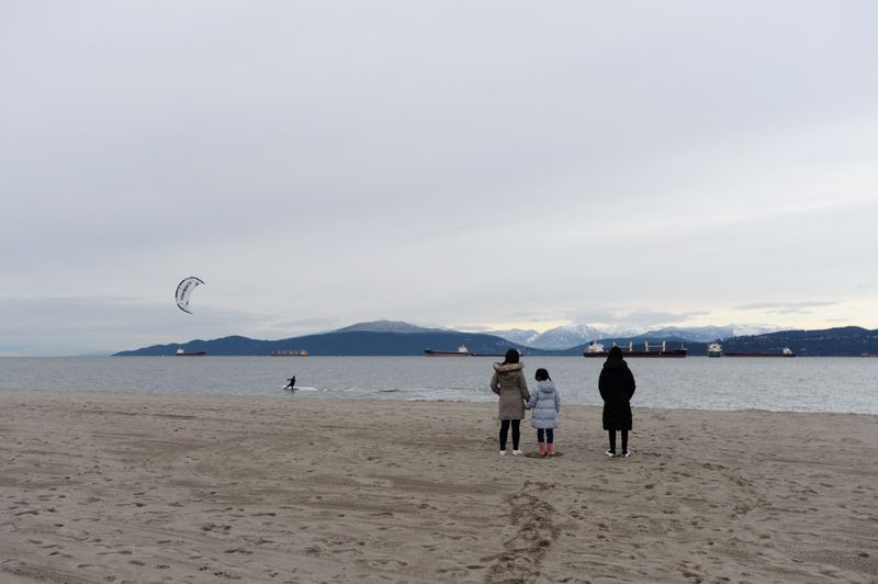 &copy; Reuters. Maria Law, who emigrated from Hong Kong with her family, watches a kite surfer with her daughters in Vancouveru000d
