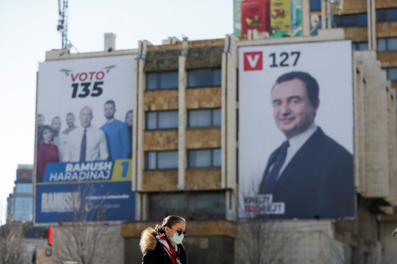 &copy; Reuters. Woman wearing a mask walks near electoral campaign billboards in Pristina