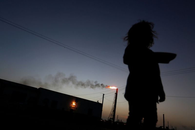 &copy; Reuters. Imagen de archivo de una niña de pie frente a su casa mientras en el fondo se ve la refinería Cardón, que pertenece a la petrolera estatal venezolana PDVSA, en Punto Fijo