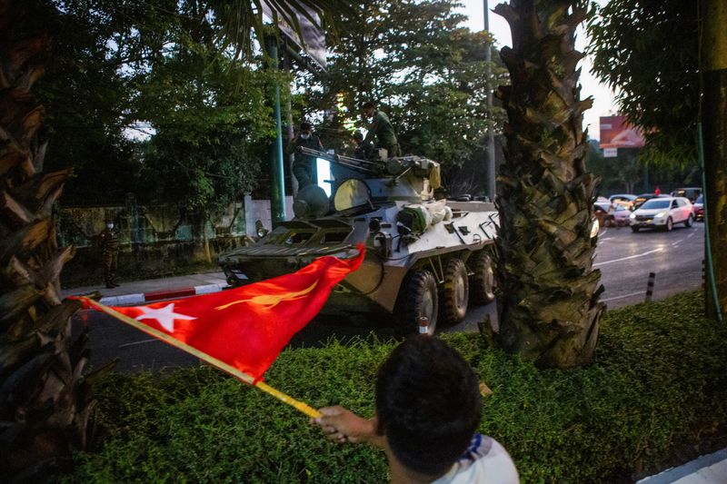 © Reuters. A man waves a flag next to an armoured vehicle in Yangon