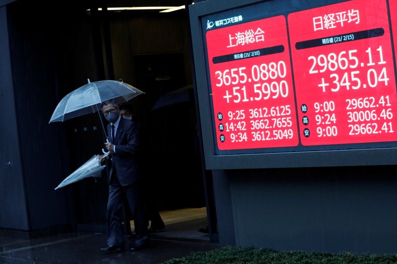 &copy; Reuters. Men holding umbrellas walk near an electric board showing Nikkei index a brokerage in Tokyo