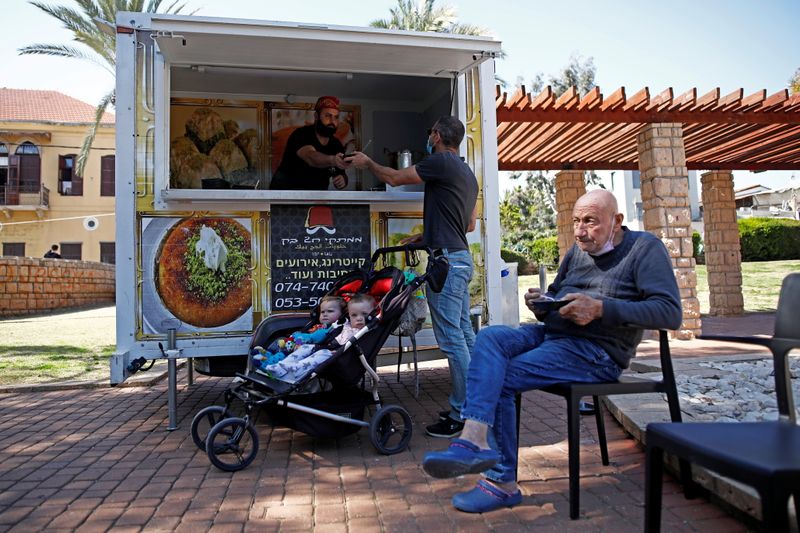 &copy; Reuters. A man receives Kanafeh, a Middle Eastern dessert, after he was vaccinated against the coronavirus disease (COVID-19), as part of an initiative to encourage people to get vaccinated, near a mobile vaccination unit in Jaffa