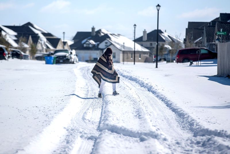 © Reuters. FILE PHOTO: A man walks to his friend's home in a neighbourhood without electricity as snow covers the BlackHawk neighborhood in Pflugerville