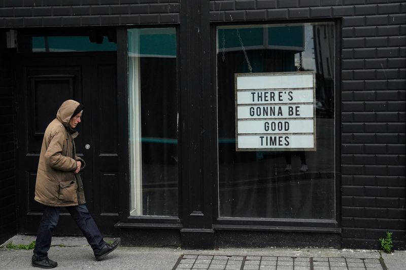 &copy; Reuters. FOTO DE ARCHIVO: Un hombre pasa caminando frente a una ventana en la que se lee &quot;Volverán los buenos tiempos&quot; en inglés en Galway