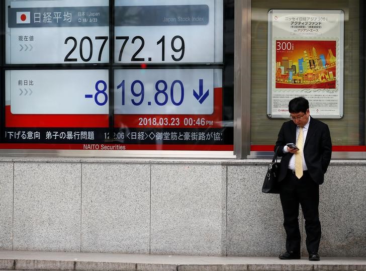 &copy; Reuters. En la imagen de archivo un hombre mira un teléfono móvil junto a una placa electrónica que muestra el promedio Nikkei de Japón fuera de una correduría en Tokio, Japón