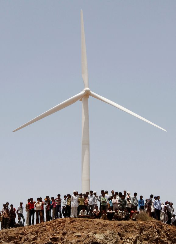 © Reuters. FILE PHOTO: Villagers stand under a power generating windmill turbine during the inauguration ceremony of the new 25 MW ReNew Power wind farm at Kalasar village