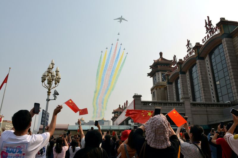 © Reuters. FILE PHOTO: People hold their mobile phones and Chinese flags as military aircraft fly in formation during the military parade marking the 70th founding anniversary of People's Republic of China, at a railway station