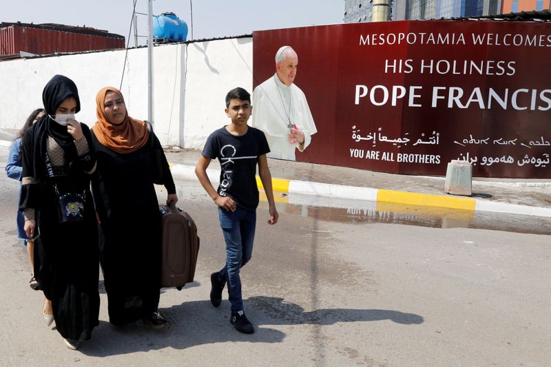 © Reuters. People walk past a poster of Pope Francis ahead of the planned visit of Pope Francis to Iraq, in Baghdad