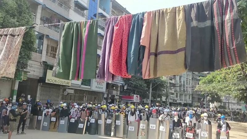 &copy; Reuters. Traditional clothes hang on a rope as protesters holds shields in the background, in Yangon