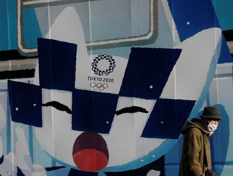 &copy; Reuters. A man wearing a protective face mask walks in front of a wall decoration featuring Tokyo 2020 Olympic Games mascot Miraitowa amid the coronavirus disease (COVID-19) outbreak in Tokyo