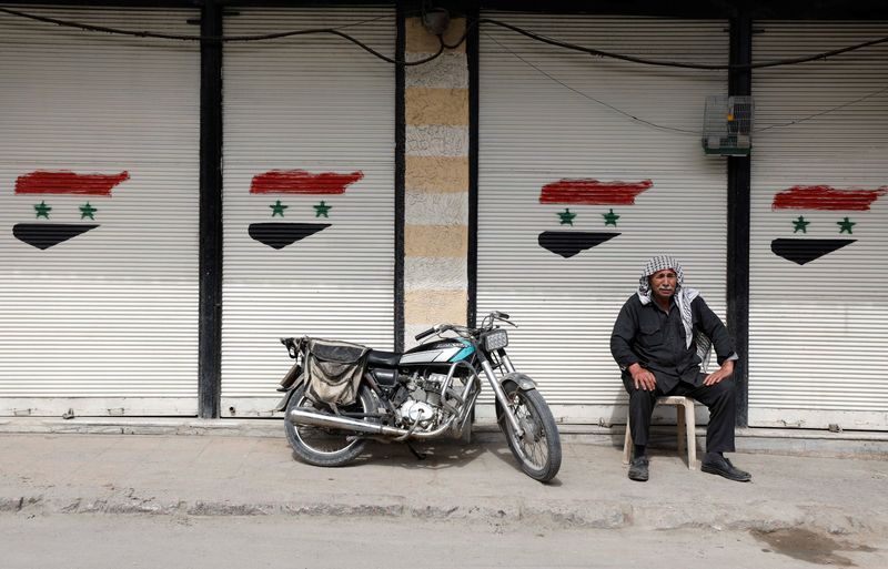 &copy; Reuters. A man sits in front of closed shop with Syrian national flags painted on their shutters in Douma